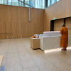 Buddhist monk in orange robes standing beside a white coffin in a peaceful modern funeral hall, with the memorial photo blurred for privacy.