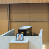 A black coffin positioned inside a modern crematorium hall, with a blurred framed memorial photograph placed in front.